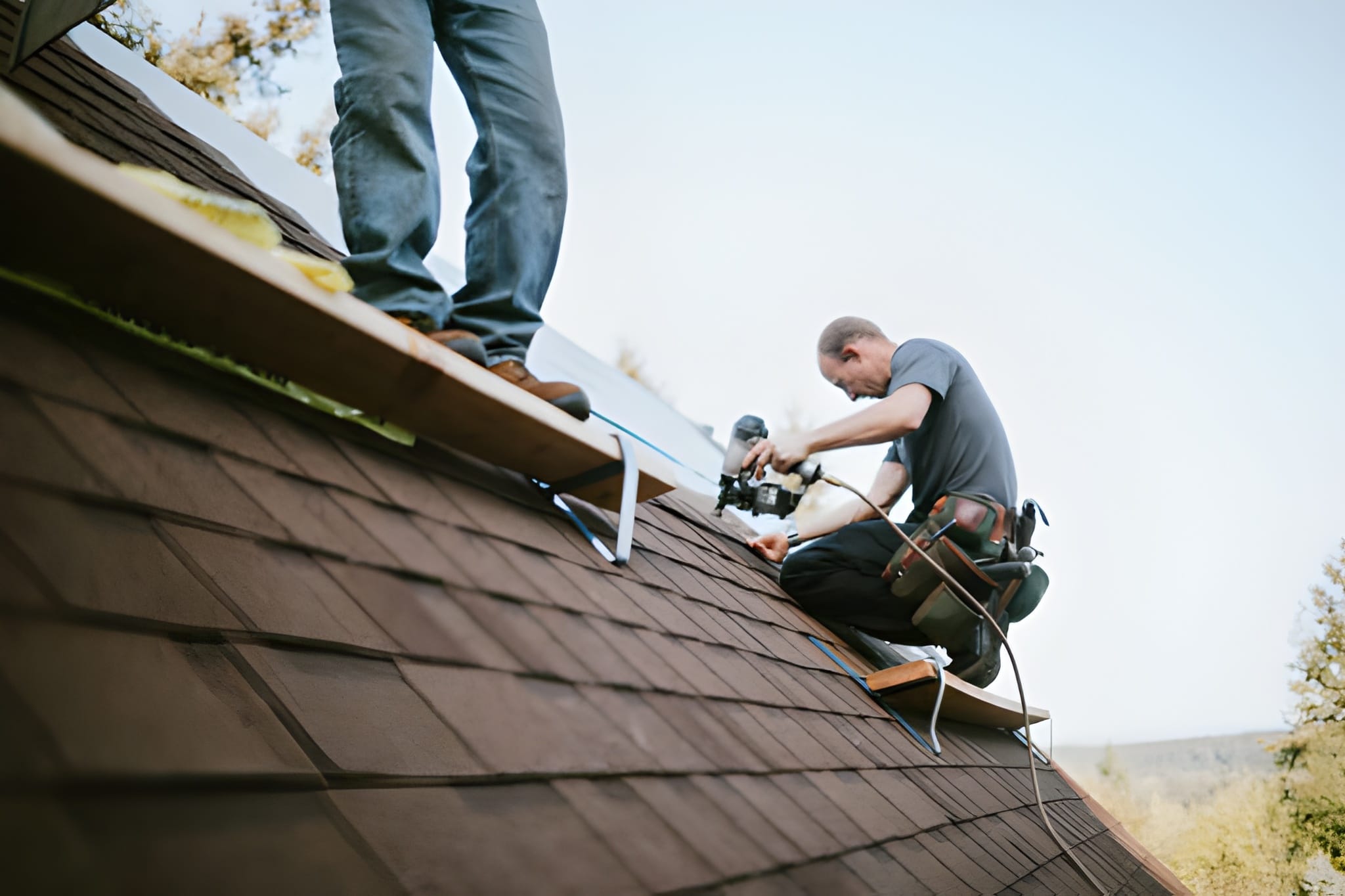 A roofer and crew work on putting in new commercial roofing shingles.